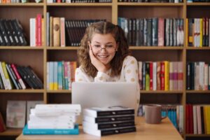 Academic Approach Tutoring and Test Prep | A girl sitting at a desk with a laptop in front of bookshelves.