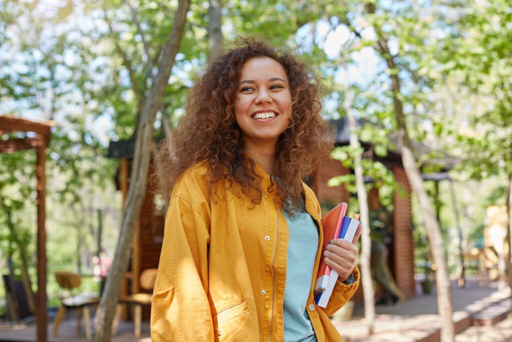 Academic Approach Tutoring and Test Prep | A young woman with curly hair standing in a park holding a book.