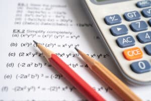 Academic Approach Tutoring and Test Prep | Two sharpened pencils, one red and one natural wood, are placed on a math worksheet next to a gray calculator. The worksheet contains algebraic equations.