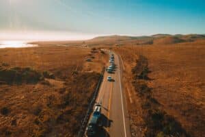 Academic Approach Tutoring and Test Prep | A long line of cars drives along a winding road through golden, grassy hills under a clear blue sky, with sunlight reflecting off the distant water to the left.