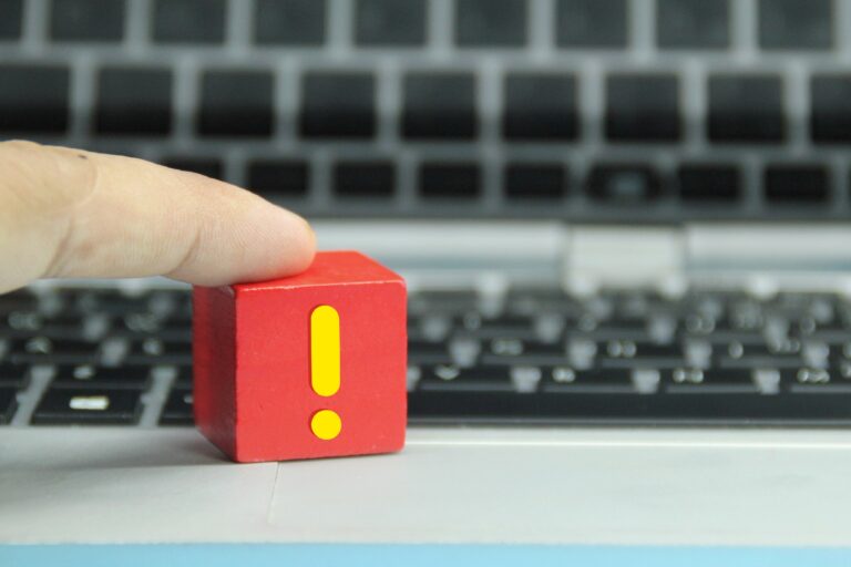 Academic Approach Tutoring and Test Prep | A hand touching a red wooden block with a yellow exclamation mark, placed on a laptop keyboard.