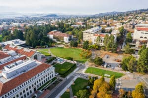 Academic Approach Tutoring and Test Prep | Aerial view of a university campus with red-roofed buildings, green lawns, trees, and cityscape in the background under a partly cloudy sky.