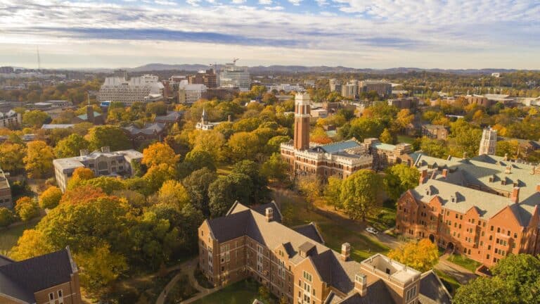 Academic Approach Tutoring and Test Prep | Aerial view of a college campus with historic buildings, green and autumn-colored trees, and a city skyline in the background under a partly cloudy sky.
